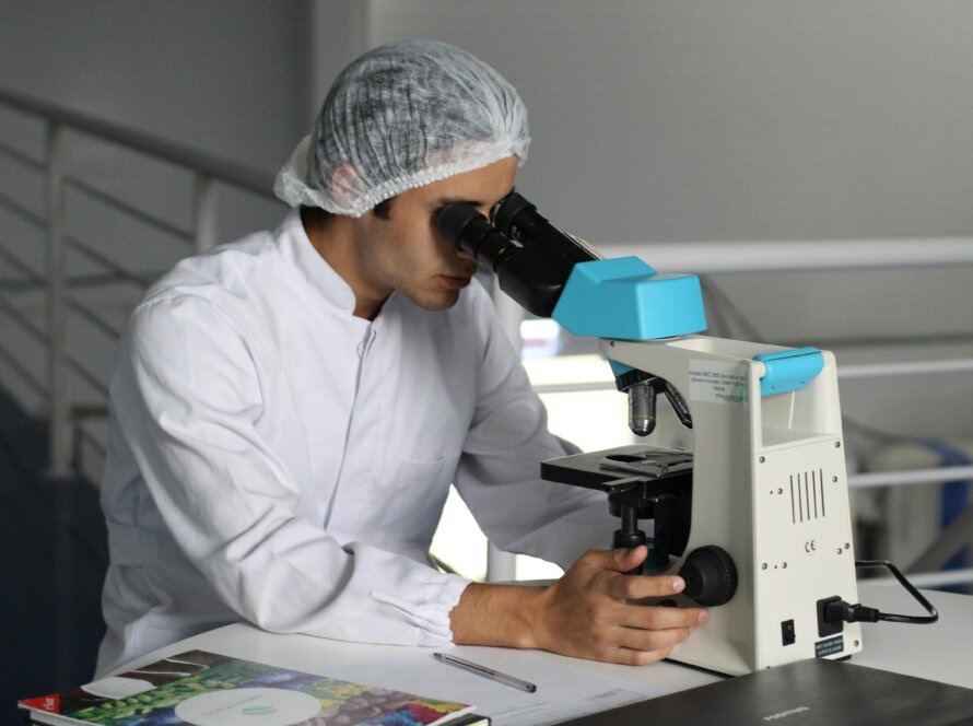 Scientist in a lab coat using a microscope to conduct research, focusing on healthcare improvements.